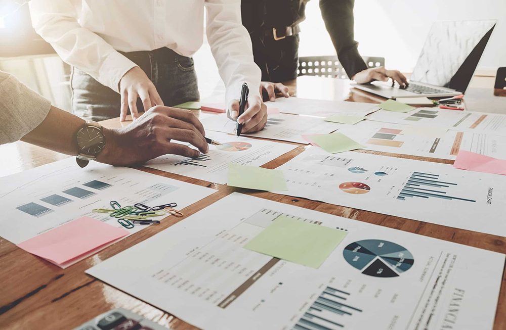 Tre regnskapskollegaer som står bøyd over bordet og diskuterer regnskap.