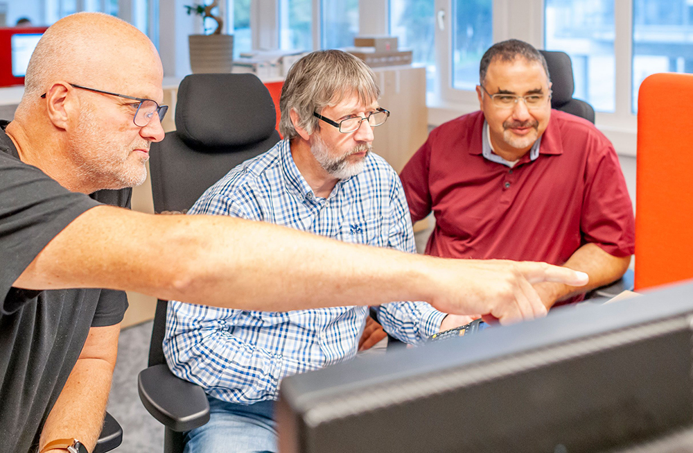 Tre kollegaer hos Wican IT som hjelper hverandre på PC'en.