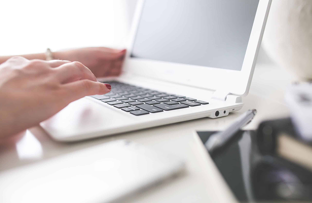 Kvinnelige hender som berører et tastatur på en laptop.