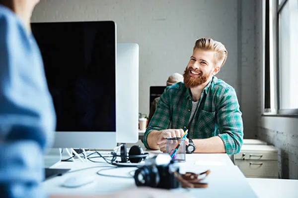 En mann som smiler til sin kollega over pulten.